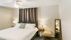 A neatly arranged hotel room with a bed, bedside lamps, a small stool, a mirror, and a ceiling fan. - Spacious 4 bed Apt with 2 Living Areas Near DT! (Libertyville)