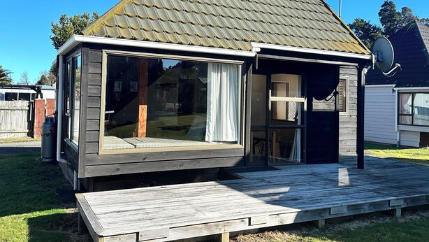A small, modern house with a sloped roof, large glass windows, and a wooden deck. - Chalet 6 - Ohakune Holiday Home (Ohakune)