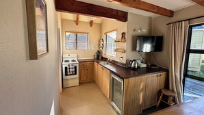 A compact kitchen with wooden cabinets, a built-in oven, a refrigerator, and a window with blinds. - Chalet 6 - Ohakune Holiday Home (Ohakune)