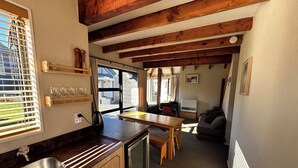 A compact kitchen with wooden beams, a sink, a refrigerator, and a dining area with a table and chairs. - Chalet 6 - Ohakune Holiday Home (Ohakune)