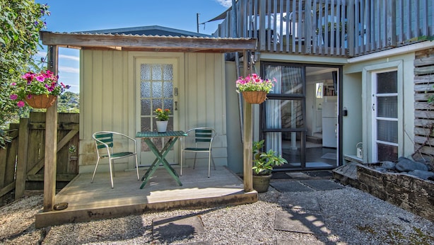 Une petite maison de plain-pied avec une terrasse en bois, un porche couvert et une porte-fenêtre coulissante donnant sur un intérieur comprenant une cuisine et un coin repas.