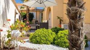 Ein Innenhof mit weißem Sonnenschirm, Gartenmöbeln und verschiedenen Pflanzen.