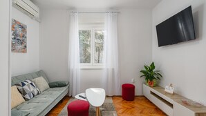 Ein modernes Wohnzimmer mit einer Couch, einem roten Hocker, einem weißen Tisch und einem an der Wand befestigten Fernseher.