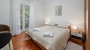 Ein Schlafzimmer mit einem Bett, einem Sessel, einem Nachttisch und einem Fenster mit Vorhängen.