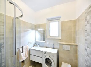 Modern bathroom with a glass-enclosed shower, sink, and front-loading washing machine.