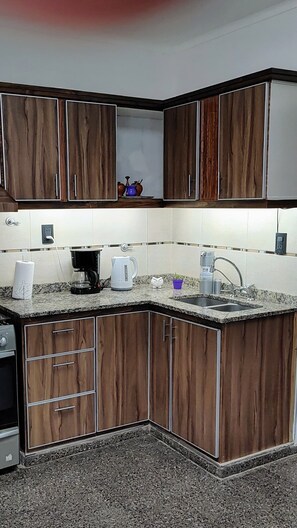 A kitchen with wooden cabinets, a granite countertop, a coffee maker, a kettle, and a sink. - A lo de Pepa - Full house, temporary family rental, in the Uco Valley (Tupungato)