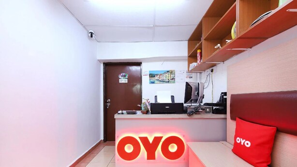A reception area with a prominent OYO logo, a reception desk, a computer, and a red pillow on a couch. - Aira Hotel Melaka (Malacca City)