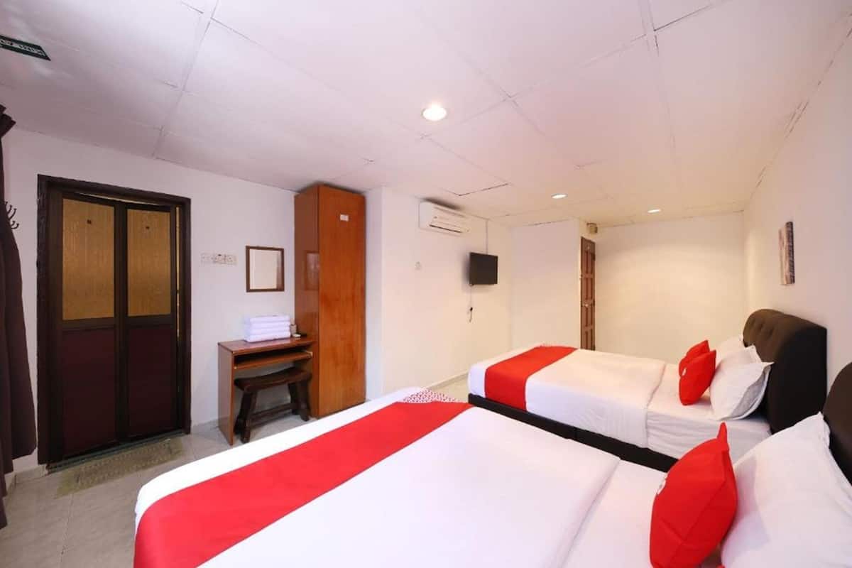 A hotel room with two beds, a wooden desk, a television, and an air conditioning unit.