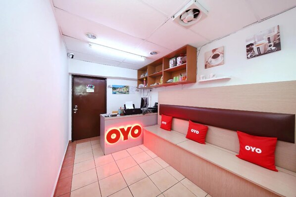 A reception area with a 'OYO' sign, a reception desk, a seating area with red cushions, and a wall with framed pictures. - Aira Hotel Melaka (Malacca City)
