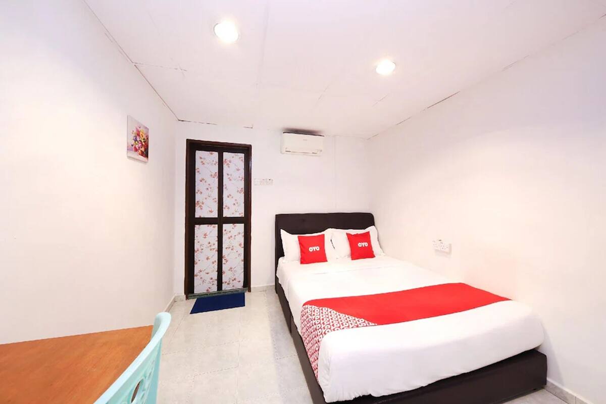 A bedroom with a bed, a door with floral wallpaper, and an air conditioning unit.