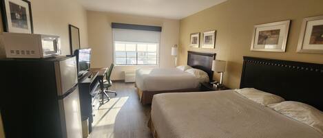 A hotel room with two beds, a desk with a computer, a microwave, and a window with a view.