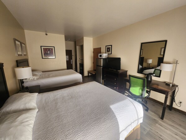 Habitación de hotel con dos camas, un escritorio con computadora, televisor, microondas y espejo.