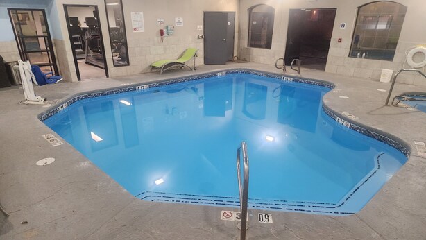 An indoor swimming pool with clear lane markings, a lifeguard chair, and a pool ladder. - CASH REWARDS INN & SUITES (Roswell)