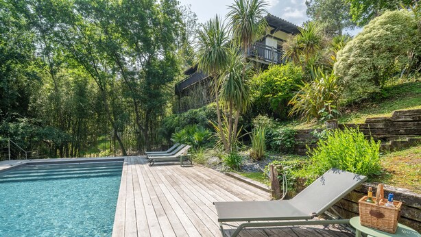 Un pontile in legno con piscina, sedie a sdraio e un cesto di vimini con bottiglie.