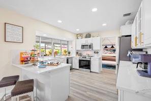 Una cocina moderna con armarios blancos, una isla central y vistas al patio trasero.