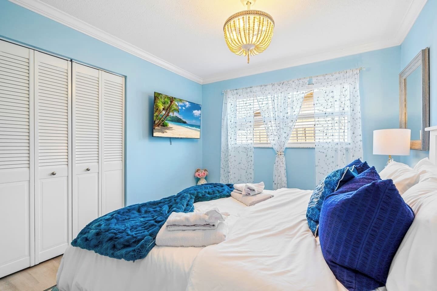 Un dormitorio con cama, candelabro, ventana con cortinas, un cuadro y armario.