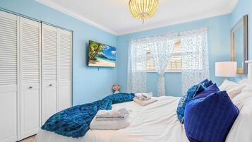 Un dormitorio con cama, candelabro, ventana con cortinas, un cuadro y armario.