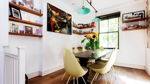 Een eetgedeelte met een tafel, stoelen en een vaas met zonnebloemen. Er zijn boekenkasten en foto's aan de muur.
