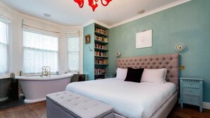 Een slaapkamer met een groot bed, een kaptafel met een badkuip, en een boekenplank.