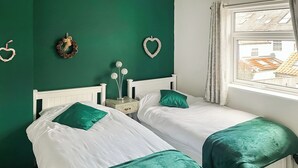 A room with two beds, green bedding, white headboards, a nightstand with a lamp, and heart-shaped wall decorations. - 2 bedroom accommodation in Beverley (Beverley)