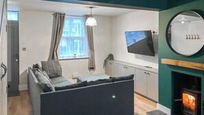 A modern living room with a sofa, a flat-screen TV, a fireplace, and a window with curtains. - 2 bedroom accommodation in Beverley (Beverley)