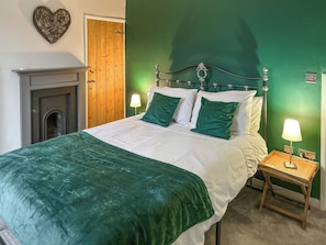 Ein Schlafzimmer mit einem Bett, grünen Kissen, einem Nachttisch mit Lampe, einer Holztür und einer herzförmigen Dekoration an der Wand.