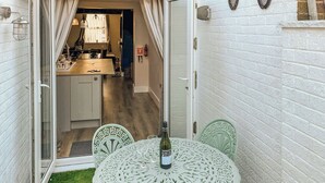 A small patio with a round table and chairs, a bottle of wine, and a view into a kitchen area. - 2 bedroom accommodation in Beverley (Beverley)