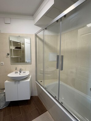 Bathroom features a glass-enclosed shower with bench and a vanity with round sink and mirror.