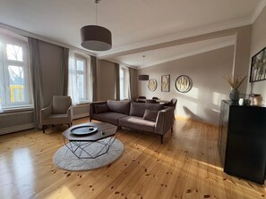 Relax in this stylish living room with a sofa, dining table, and console table, featuring decorative art and a vase with dried plants.