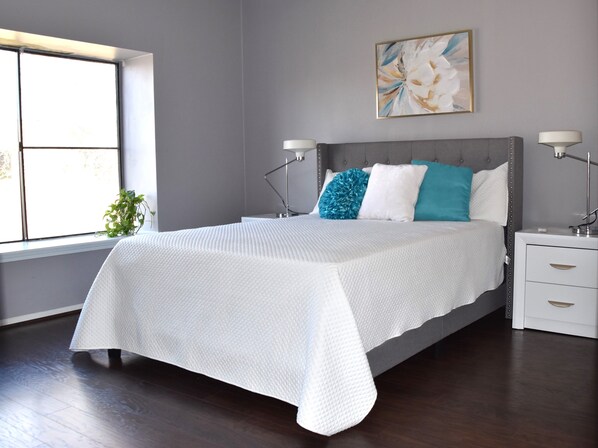 Une chambre moderne avec un grand lit, des murs gris, une fenêtre et un tableau.