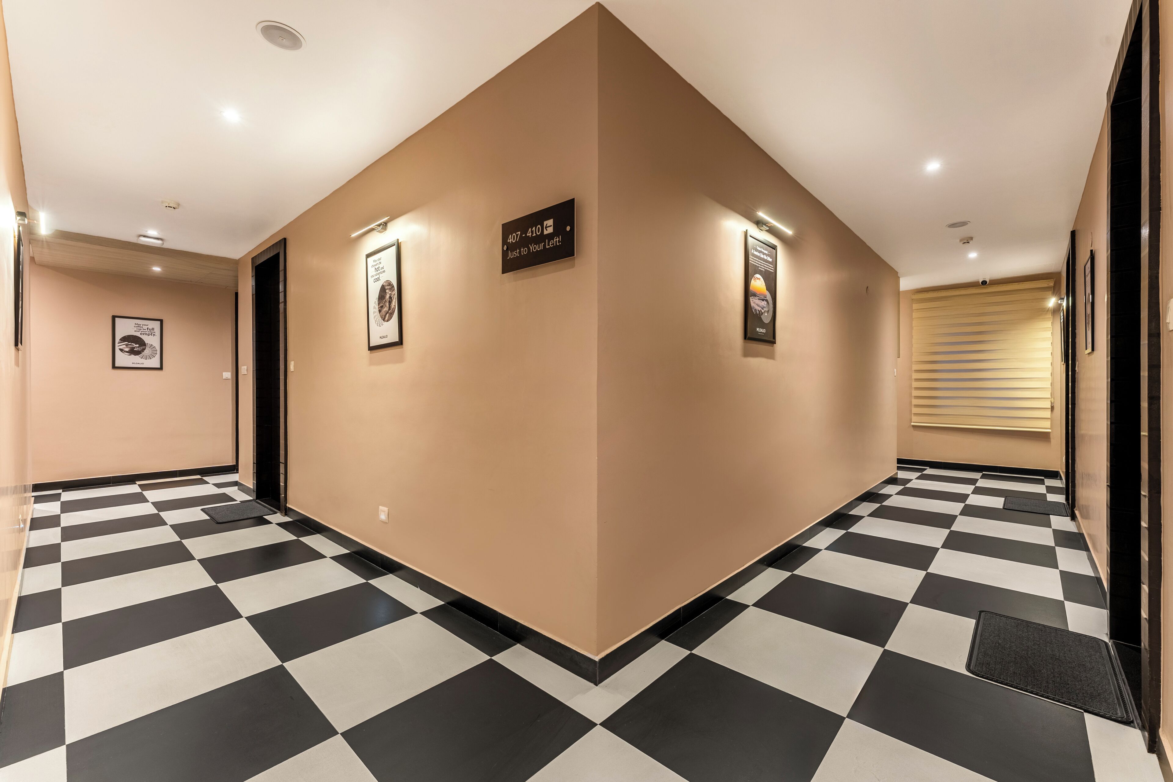 A hotel hallway with a checkered floor, beige walls, and framed pictures.
