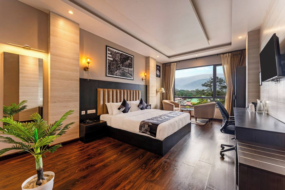 Quarto de hotel moderno com uma cama grande, uma mesa e vista para as montanhas.