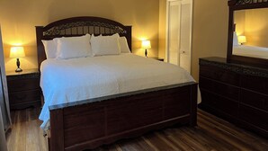 A neatly made bed with a wooden headboard, two bedside lamps, a ceiling fan, and a mirror above a dresser.
