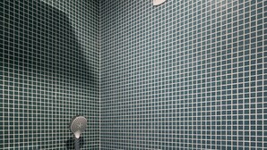 Un bagno con parete rivestita di piastrelle, un soffione doccia e una piccola mensola.