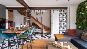 A modern living space with a wooden dining table, teal and green chairs, a wooden coffee table, and a gray sofa with a brown throw.