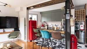 A modern kitchen with a central island, bar stools, a red refrigerator, and a TV mounted on the wall.