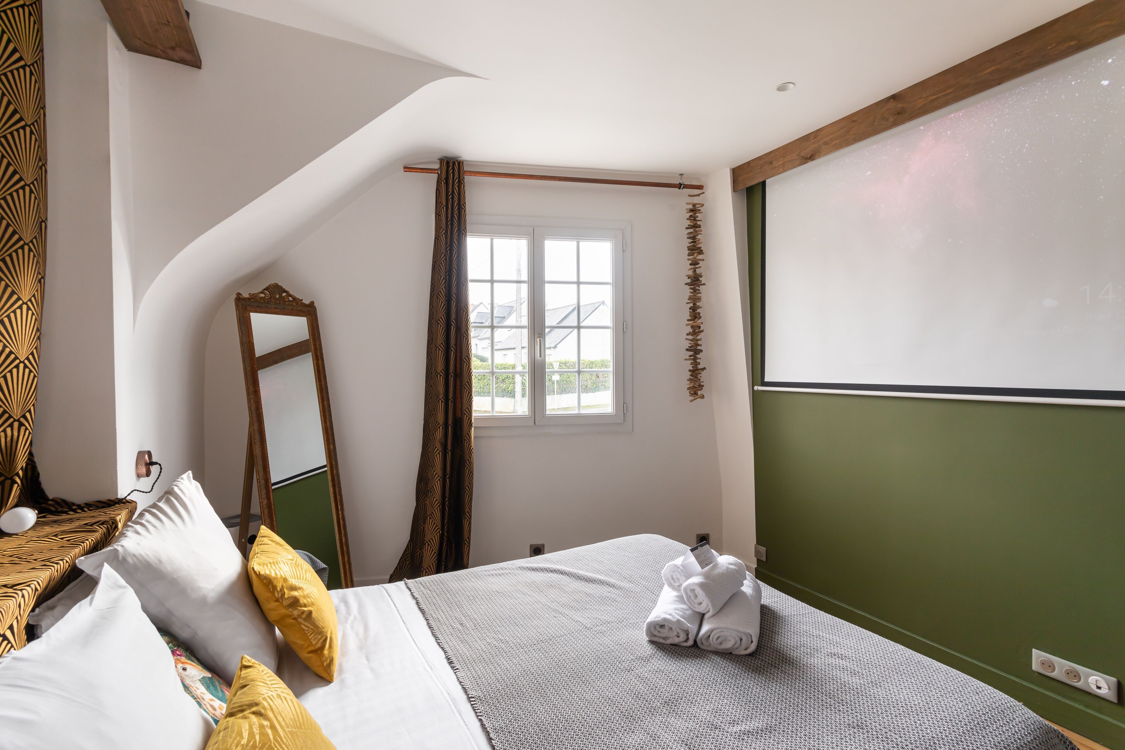 Un dormitorio con cama, almohadas, un espejo, una ventana y una pared verde.
