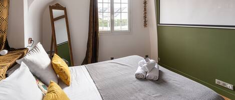 Un dormitorio con cama, almohadas, un espejo, una ventana y una pared verde.