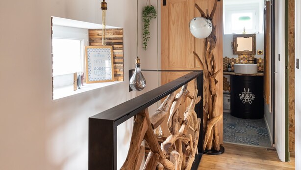 A hallway with a wooden floor, a black railing, and a mirror on the wall.