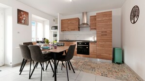 A modern kitchen with wooden cabinets, a stainless steel range hood, and a dining area with a table and chairs. - La Caulnaise - Maison climatisée avec terrasse (Caulnes)