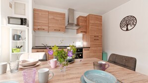 A modern kitchen with wooden cabinets, a stainless steel range hood, and a dining area with a wooden table set for four. - La Caulnaise - Maison climatisée avec terrasse (Caulnes)