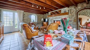 Una sala de estar acogedora con paredes de piedra, vigas de madera, sillones de cuero, chimenea y una mesa de comedor con aperitivos.