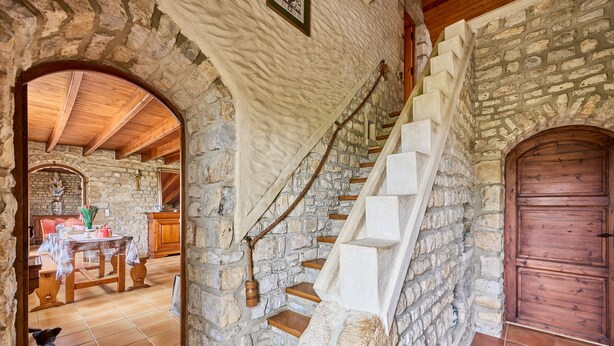 Una escalera de piedra que conduce a una puerta de madera, un comedor con mesa y sillas, y un interior rústico con paredes de ladrillo visto.