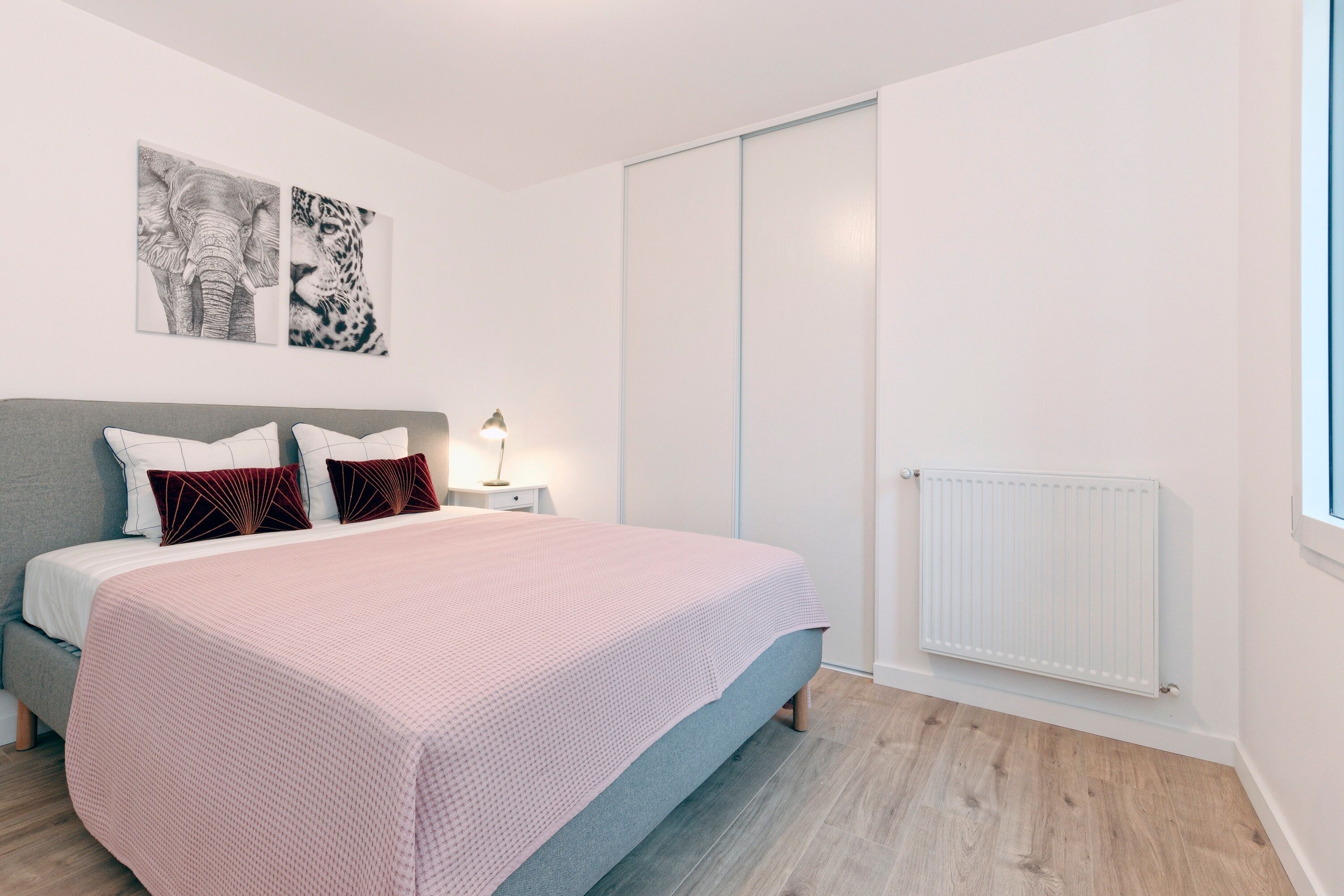 Une chambre à coucher avec un lit, des oreillers, une table de chevet, une lampe et deux œuvres d’art murales.