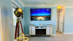 Un salon avec un téléviseur fixé au mur qui diffuse l’émission « The Spa », une cheminée, une lampe et un trépied avec un projecteur.