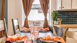 Une table à manger dressée pour quatre personnes, avec des serviettes orange, des verres remplis de glaçons et une vue sur une clôture en bois et des oiseaux à l’extérieur.