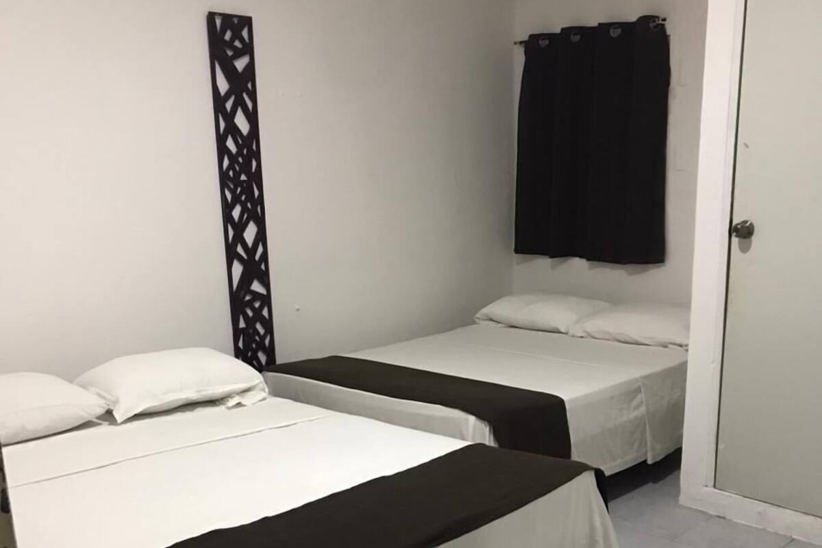 A room with two beds, a black decorative panel, a white air conditioning unit, and a black curtain.