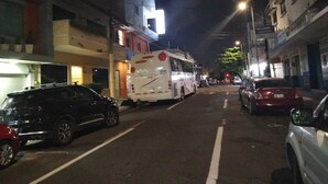 Une rue de nuit, avec des voitures garées et un autobus. Des immeubles bordent la rue, certains arborent des enseignes.