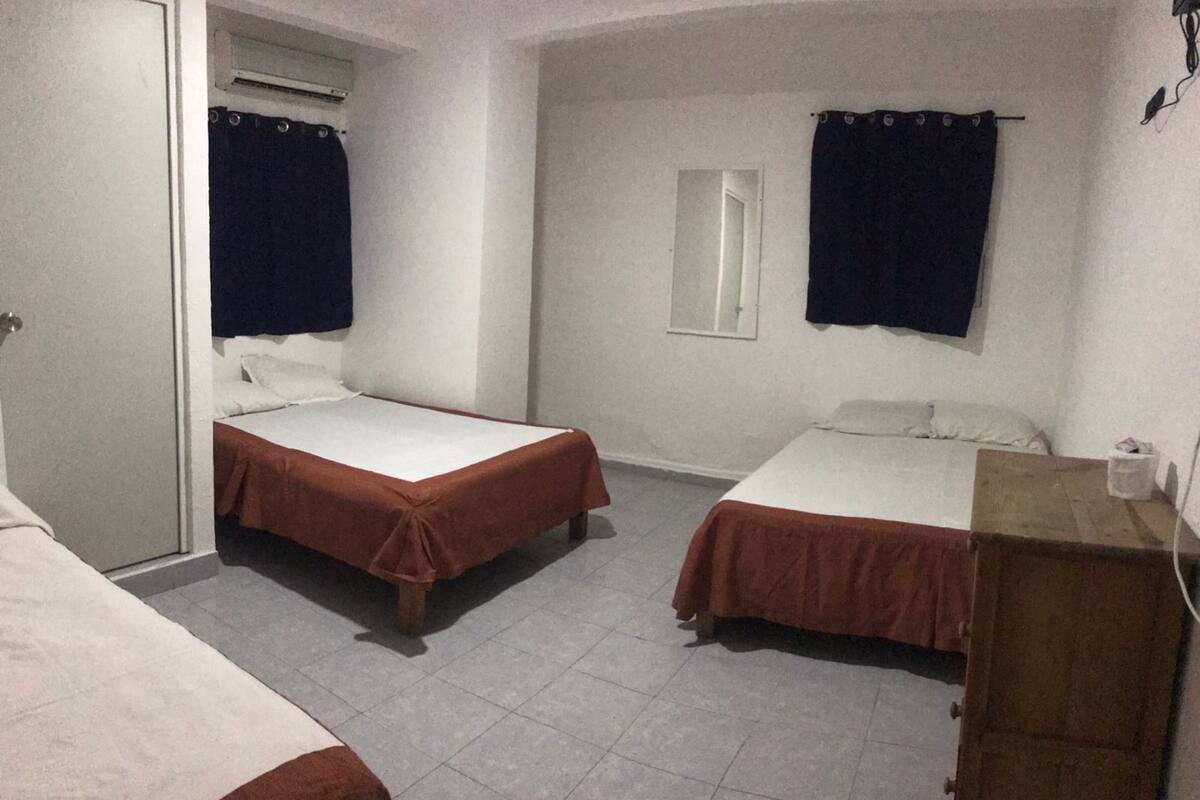 A room with two single beds, a wooden dresser, a mirror, and a window with curtains.