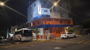 Un hôtel avec une enseigne bien visible indiquant « HÔTEL », un arrêt de bus et une voiture garée devant.